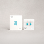 Blue gummy bear earrings on display with Teddi Lab packaging on a gray background
