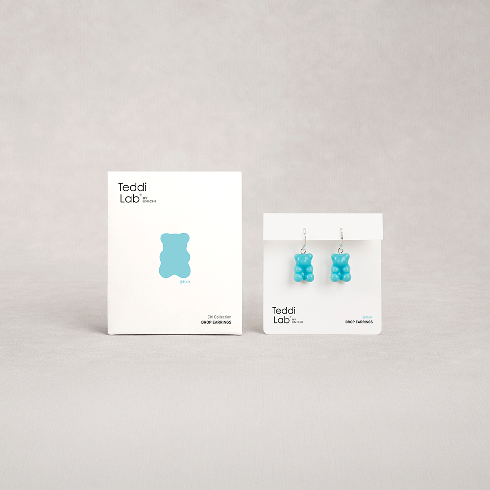 Blue gummy bear earrings on display with Teddi Lab packaging on a gray background