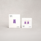 Purple gummy bear earrings on display with a branded card against a gray background