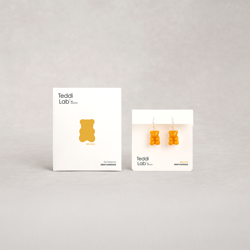Two packages of 'Teddi Lab' gummy bear-shaped earrings on a light gray background